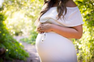 Pregnant lady with her arms crossed over her stomach while standing in the woods