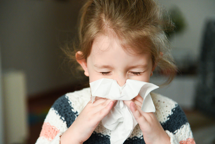 little girl sneezing into tissue